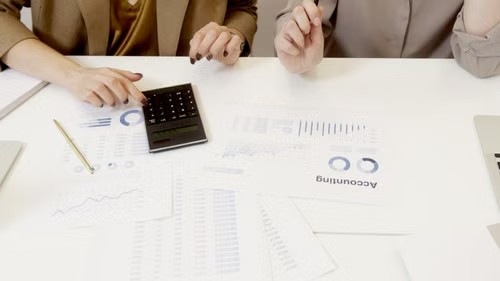 Dos personas trabajando en un escritorio con una calculadora y documentos financieros