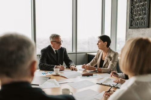 Grupo de profesionales sentados alrededor de una mesa de conferencias en una oficina luminosa, discutiendo documentos