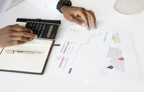 Manos trabajando con una calculadora y un documento financiero con un mapa y gráficos