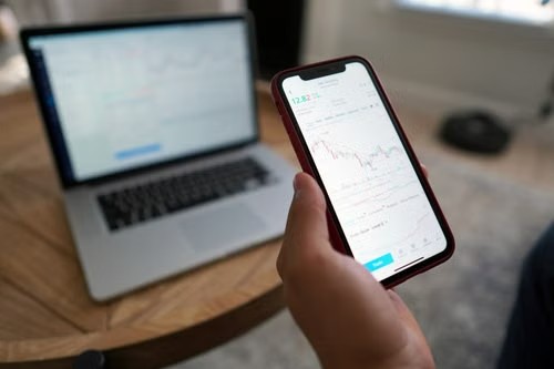 Persona revisando gráficas financieras en un smartphone junto a un portátil