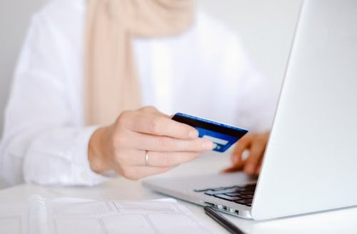 Persona trabajando en un portátil mientras sostiene una tarjeta de crédito