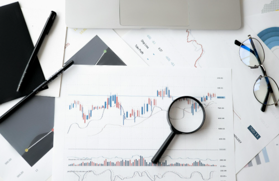 Gráficos financieros con lupa, gafas y portátil sobre el escritorio